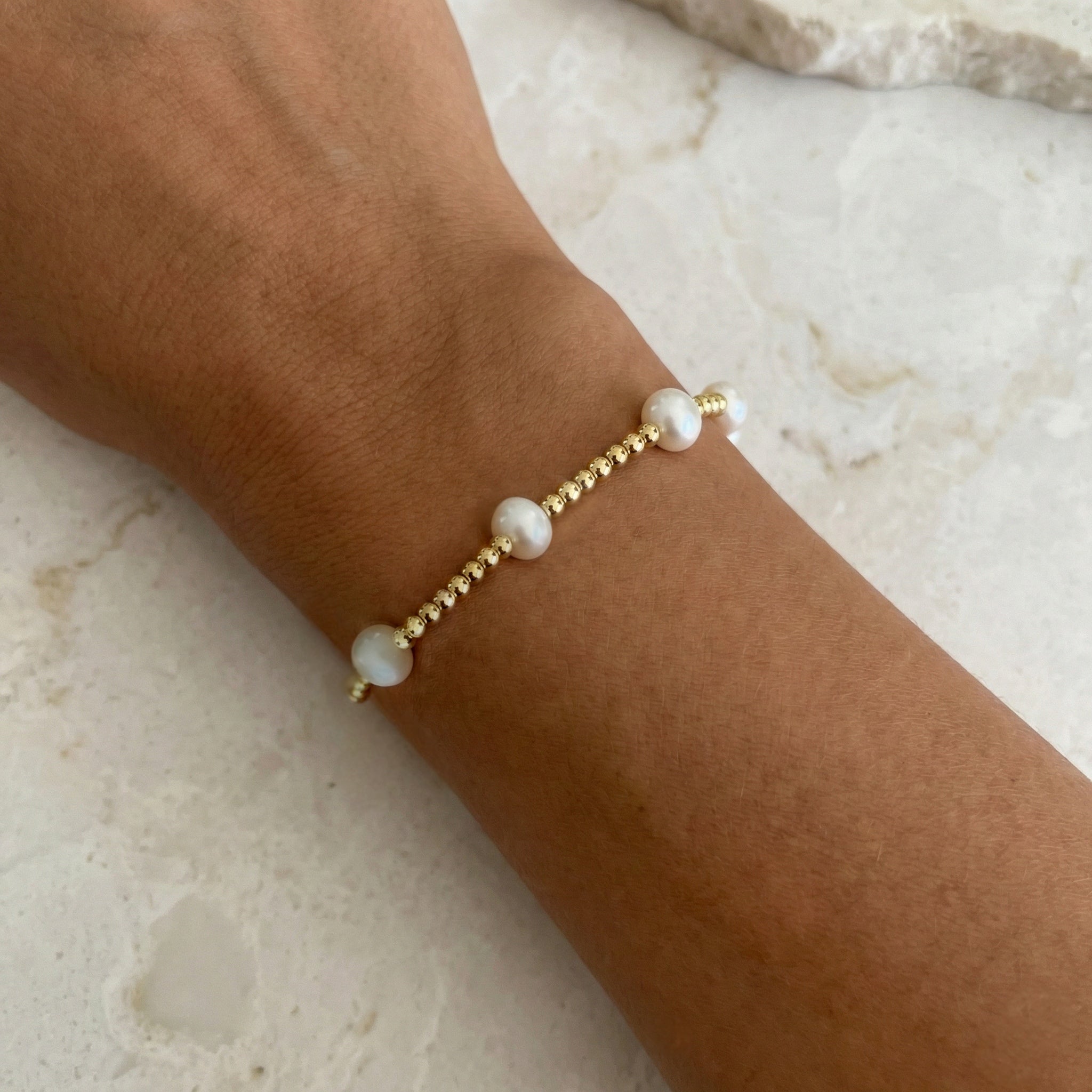 Gold beaded bracelet with pearls on a wrist against a marble background
