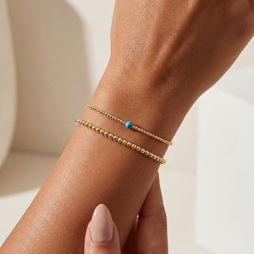 Gold bracelet with a blue gemstone on a wrist against a neutral background