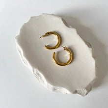 Gold hoop earrings on a white stone surface