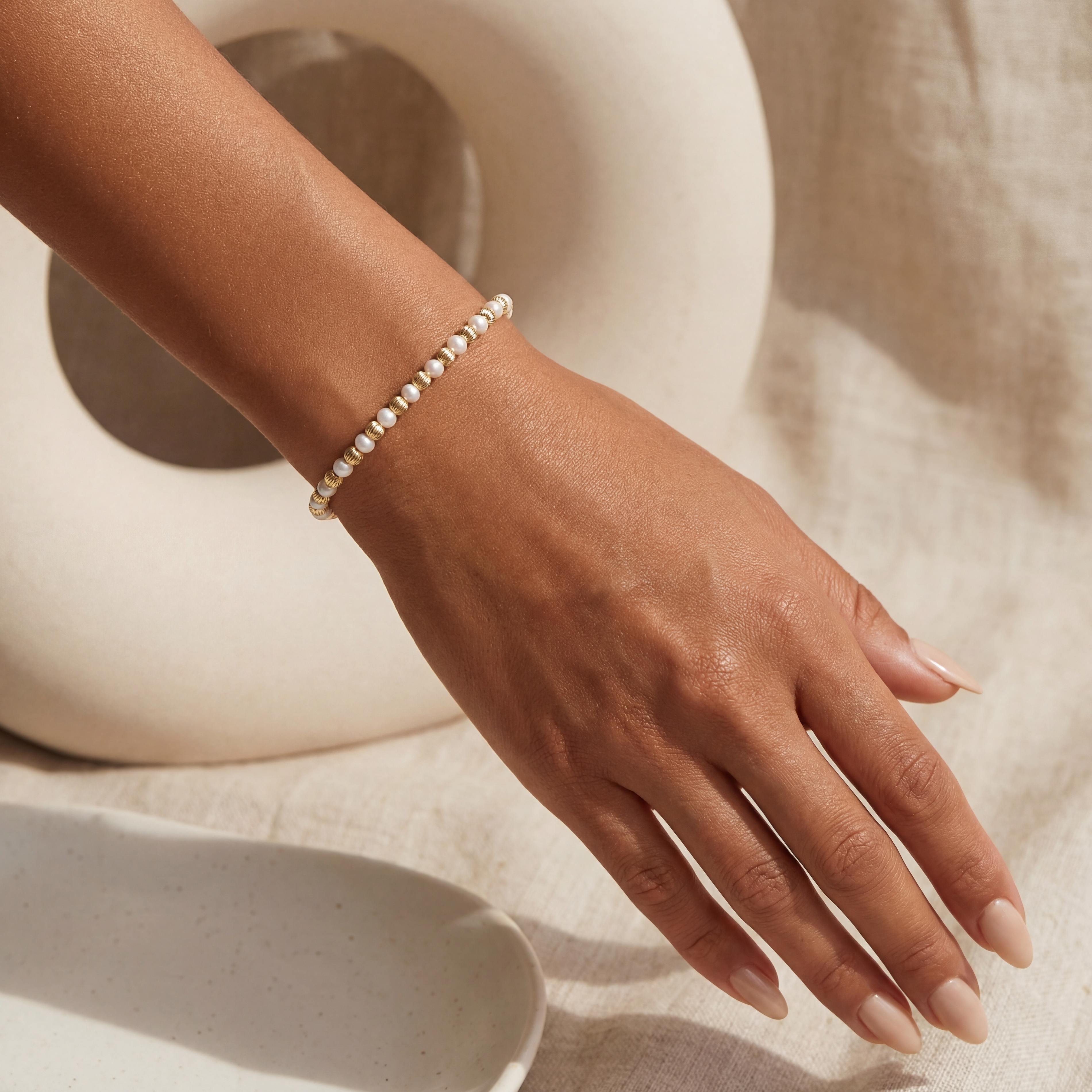 Hand wearing a pearl beaded bracelet on a neutral background