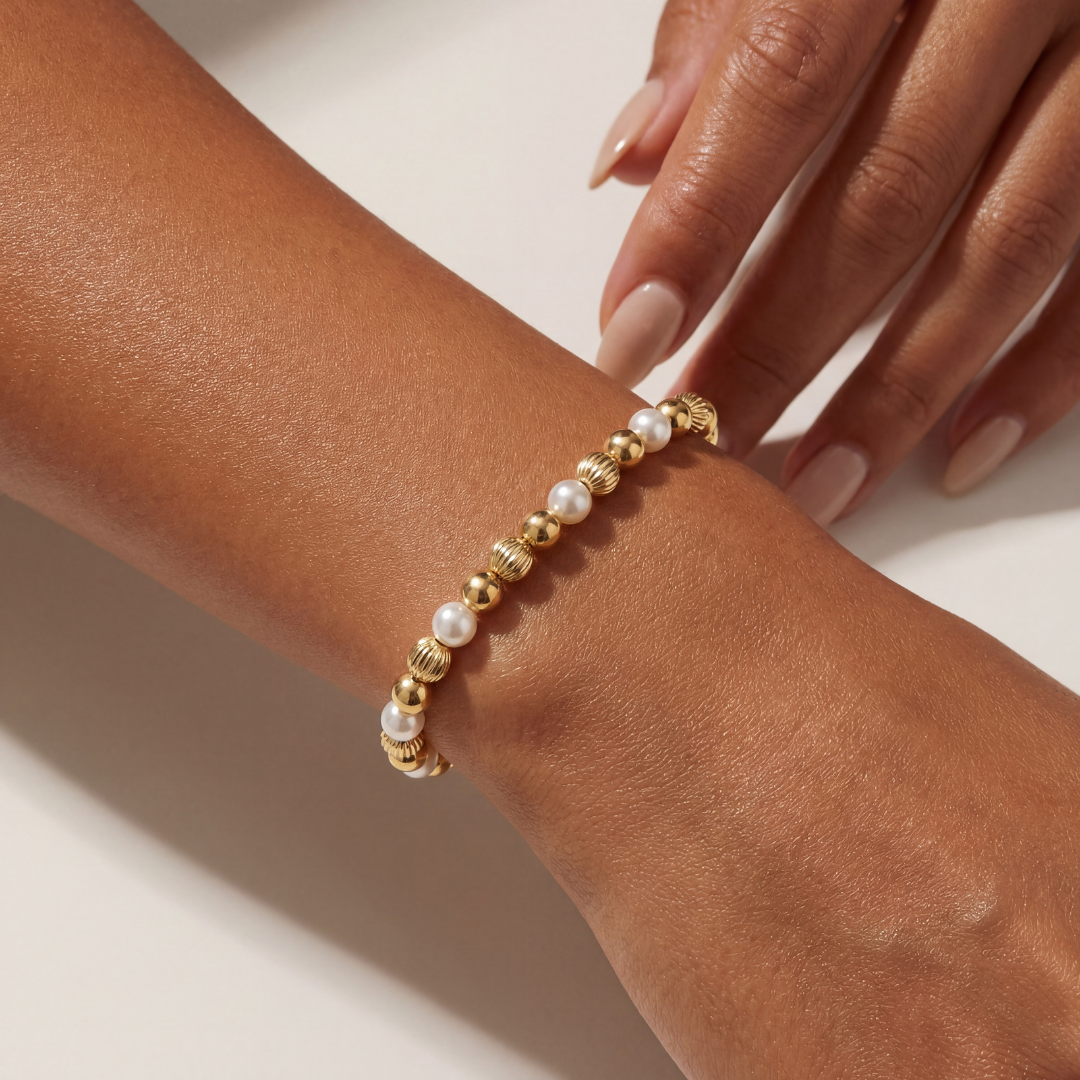 Gold and pearl beaded bracelet on a wrist with a neutral background