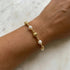 Gold and pearl bracelet on a wrist against a marble background