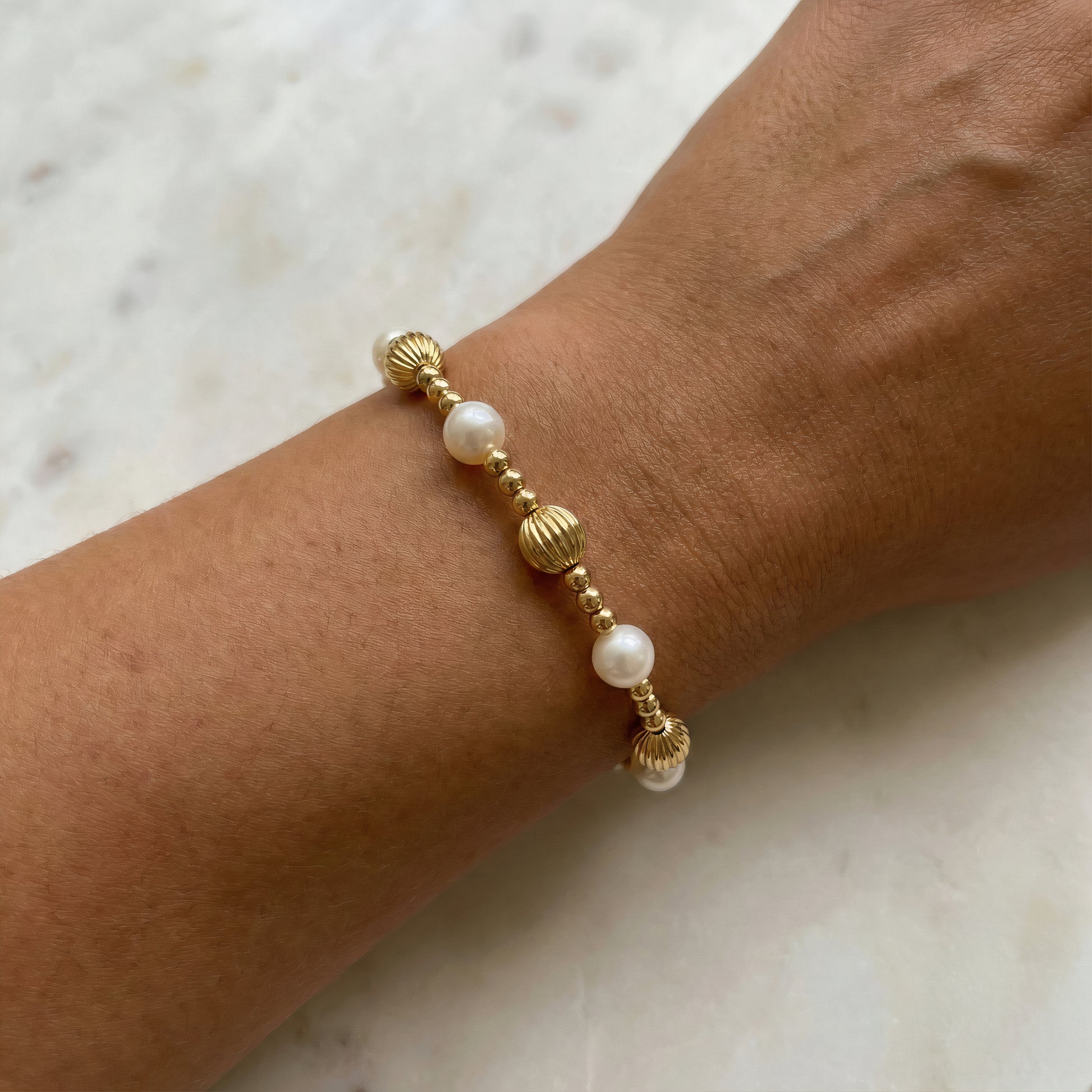 Gold and pearl bracelet on a wrist against a marble background