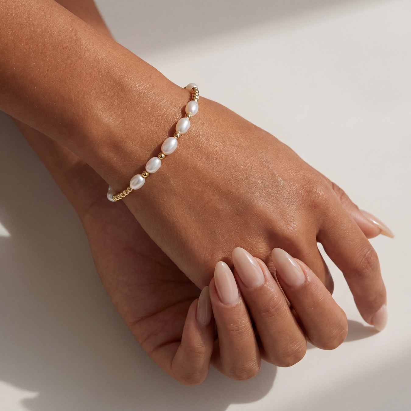 Hand wearing a pearl beaded bracelet on a neutral background