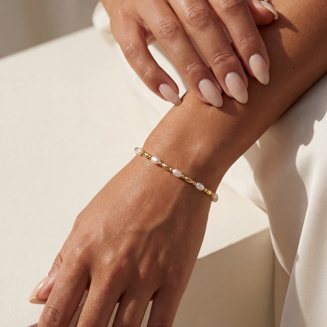Hand wearing a gold beaded bracelet with pearls on a light background