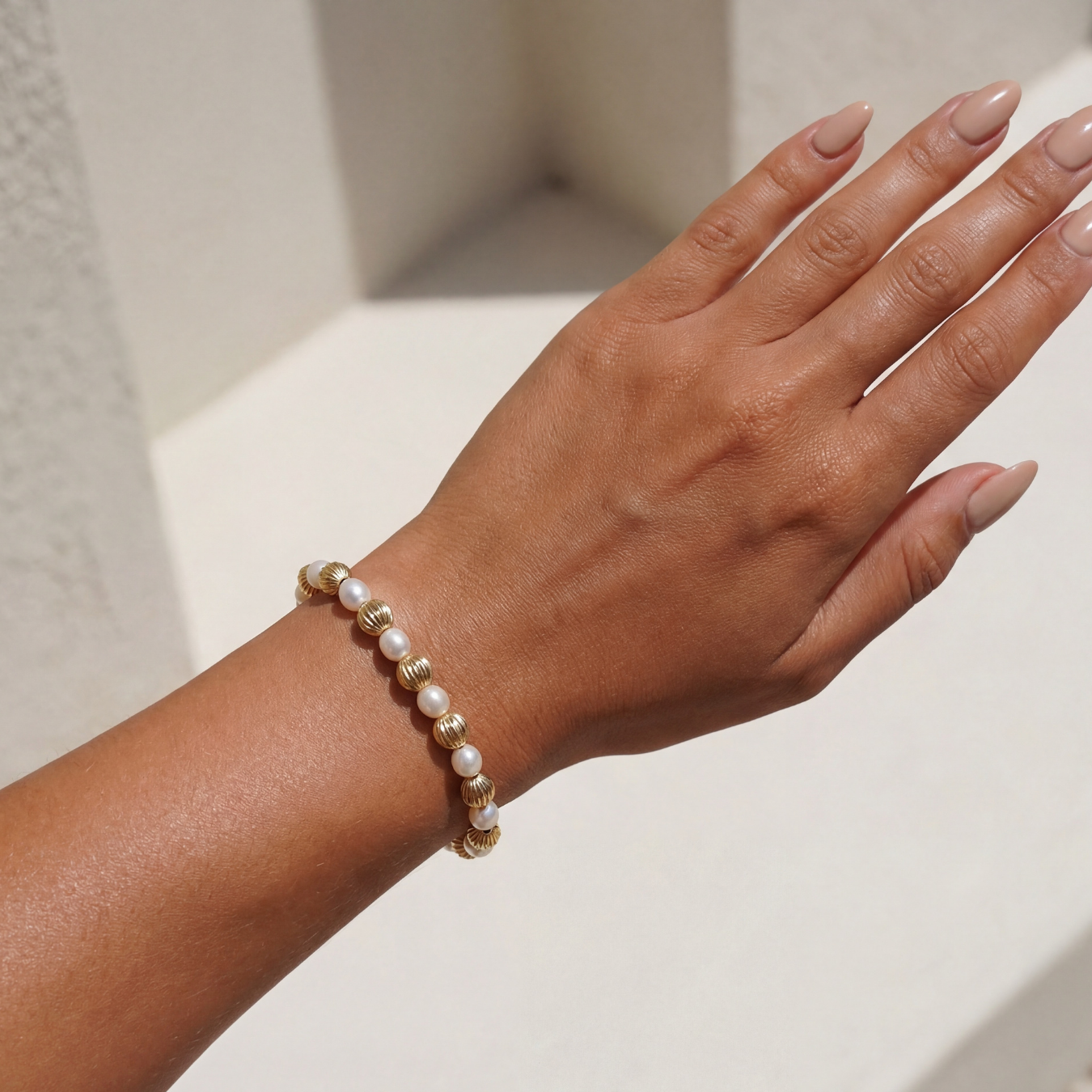 Hand wearing a pearl beaded bracelet on a neutral background
