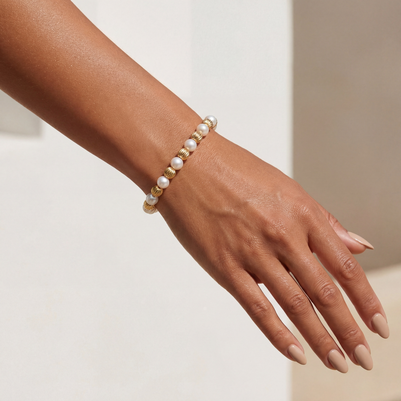 Hand wearing a pearl and gold beaded bracelet on a neutral background