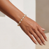 Hand wearing a pearl and gold beaded bracelet on a neutral background