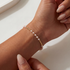 Close-up of a hand wearing a pearl beaded bracelet on a neutral background