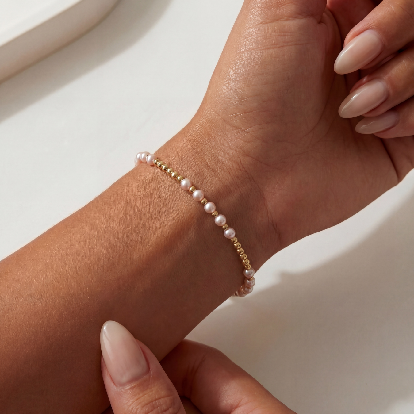 Close-up of a hand wearing a pearl beaded bracelet on a neutral background