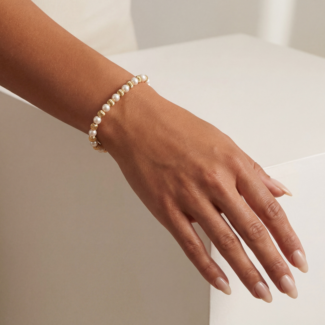 Hand wearing a pearl beaded bracelet on a neutral background