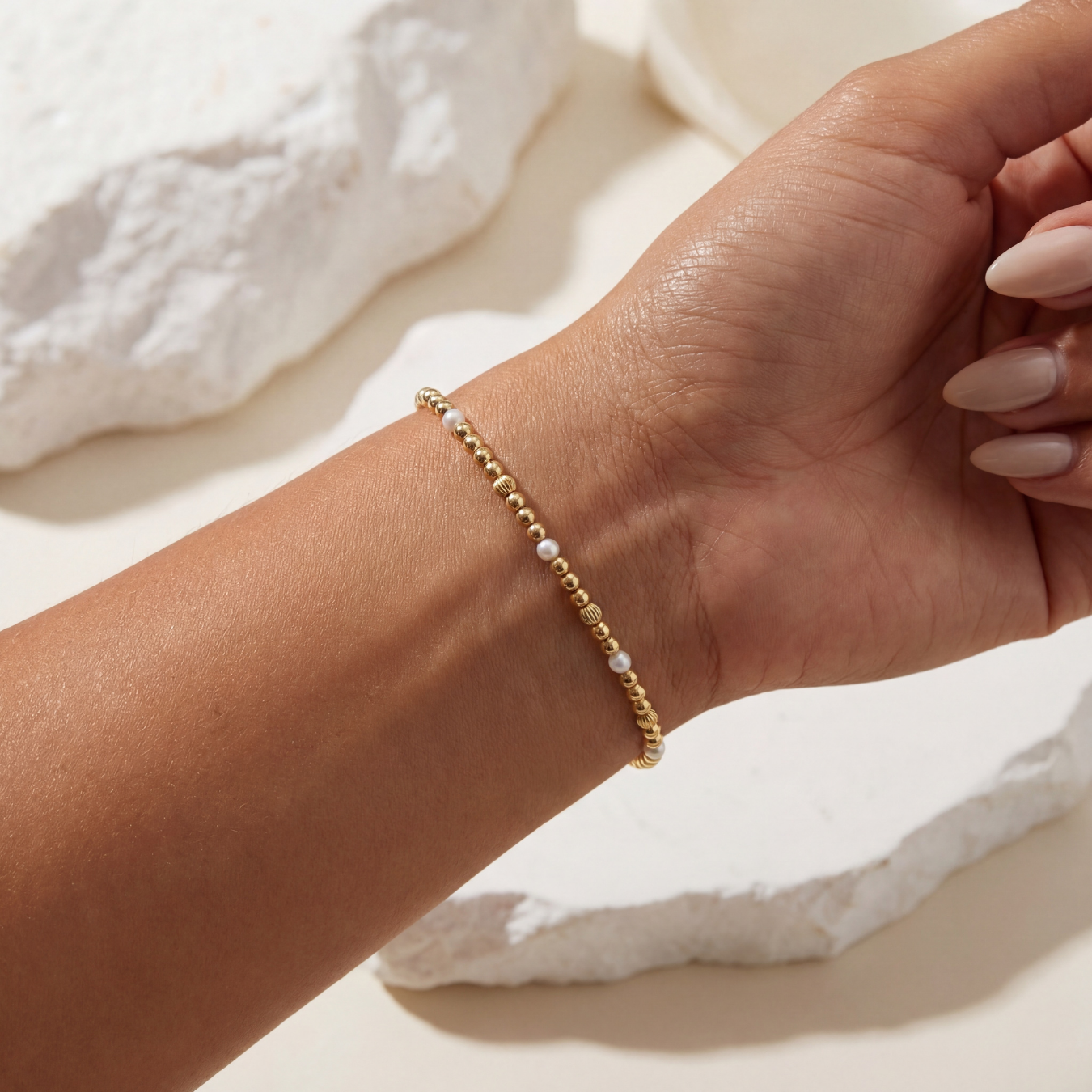 Gold beaded bracelet on a wrist with a soft white background