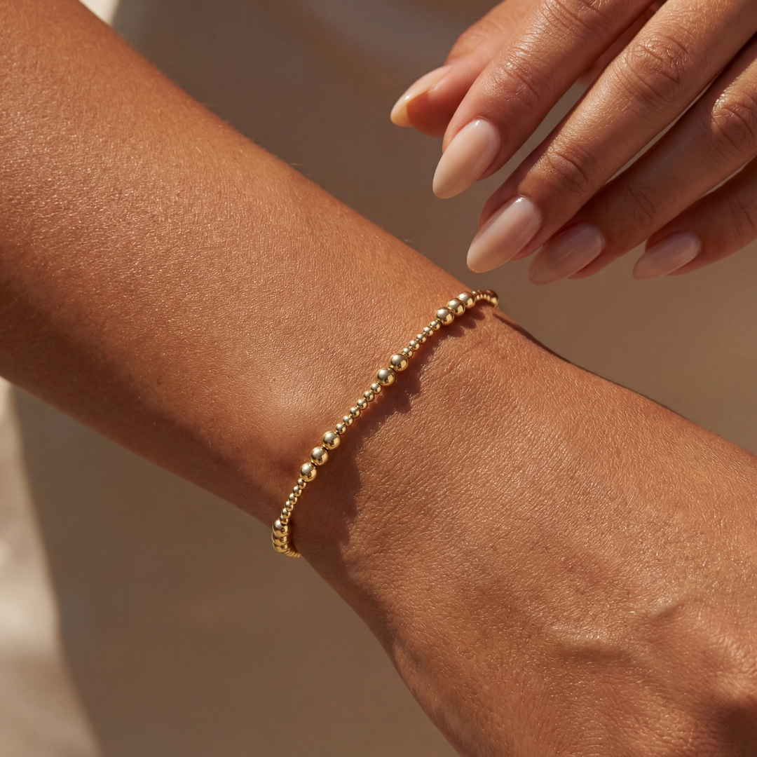 Gold beaded bracelet on a wrist with a blurred background