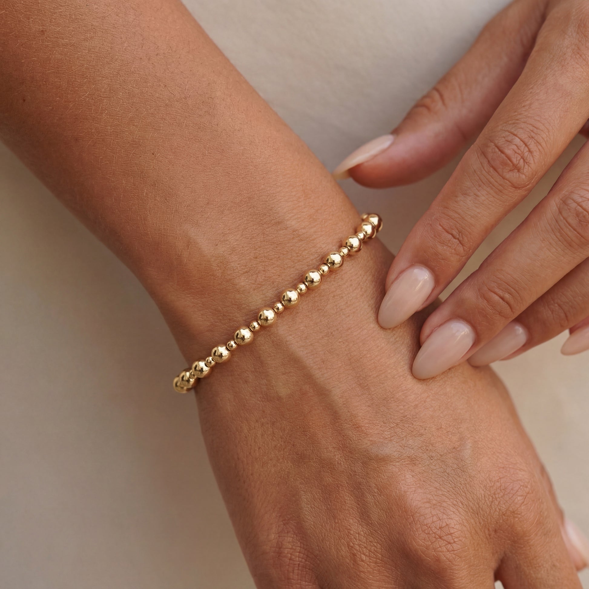 Gold beaded bracelet on a wrist with a neutral background