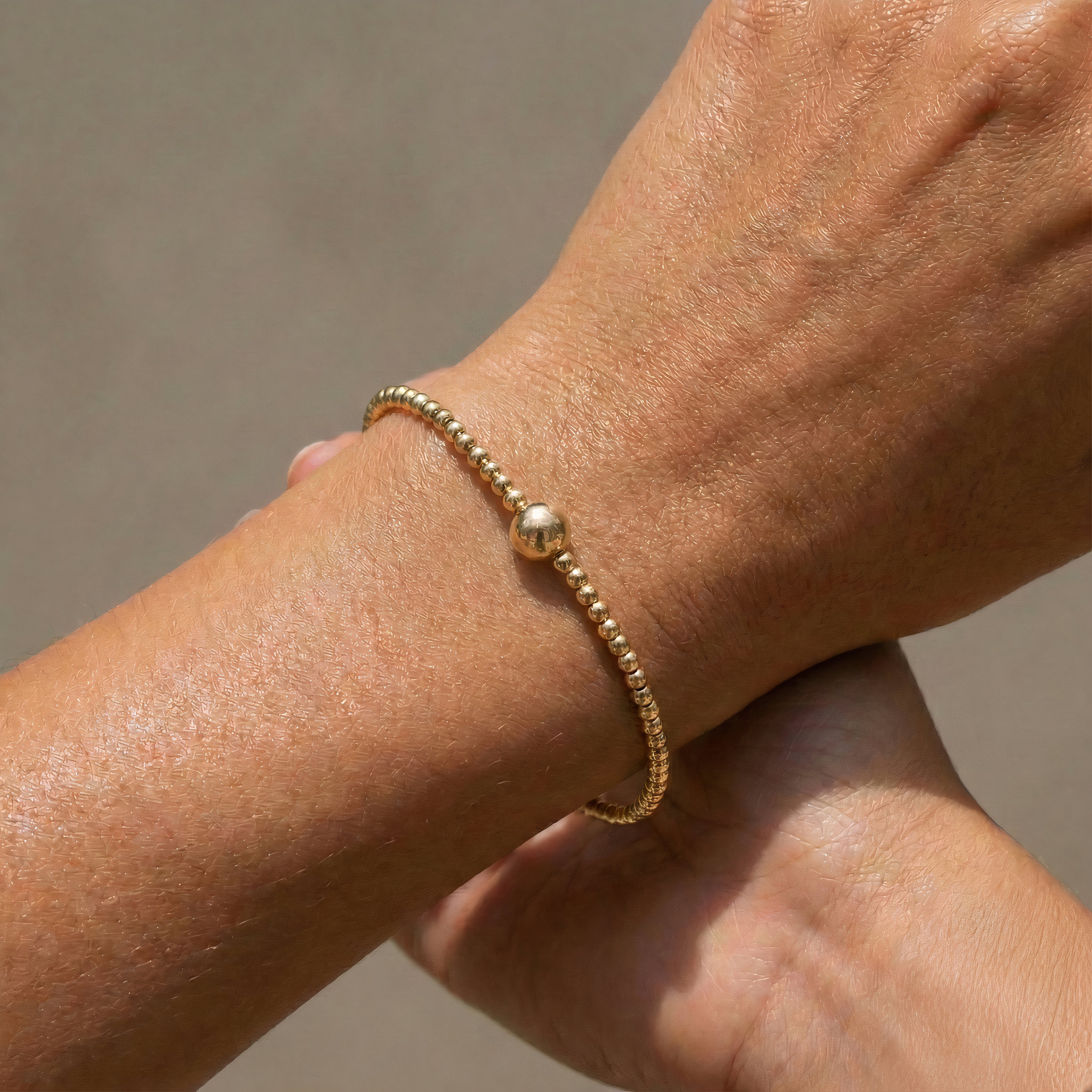 Gold beaded bracelet on a wrist against a neutral background