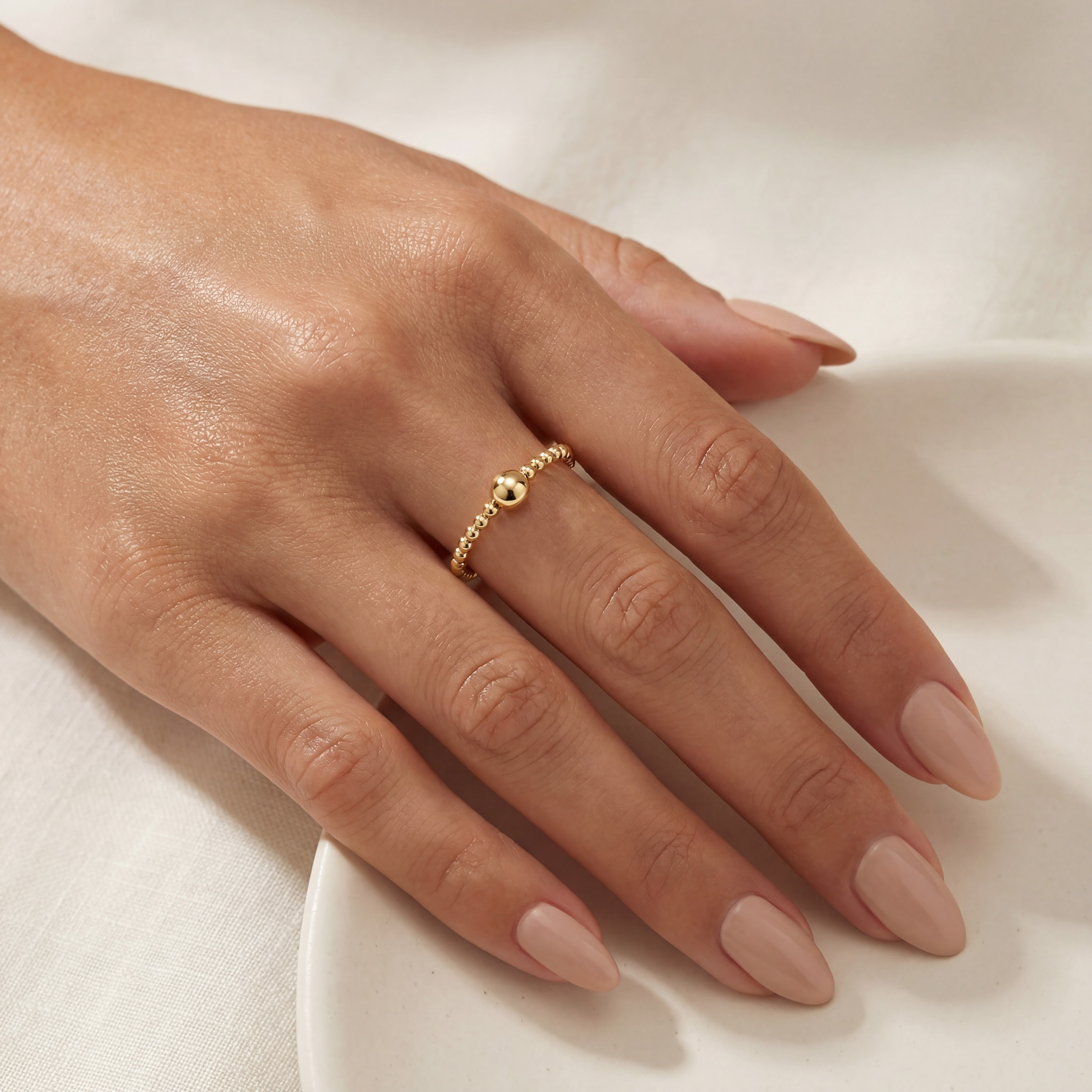 Hand wearing a gold beaded ring on a light background