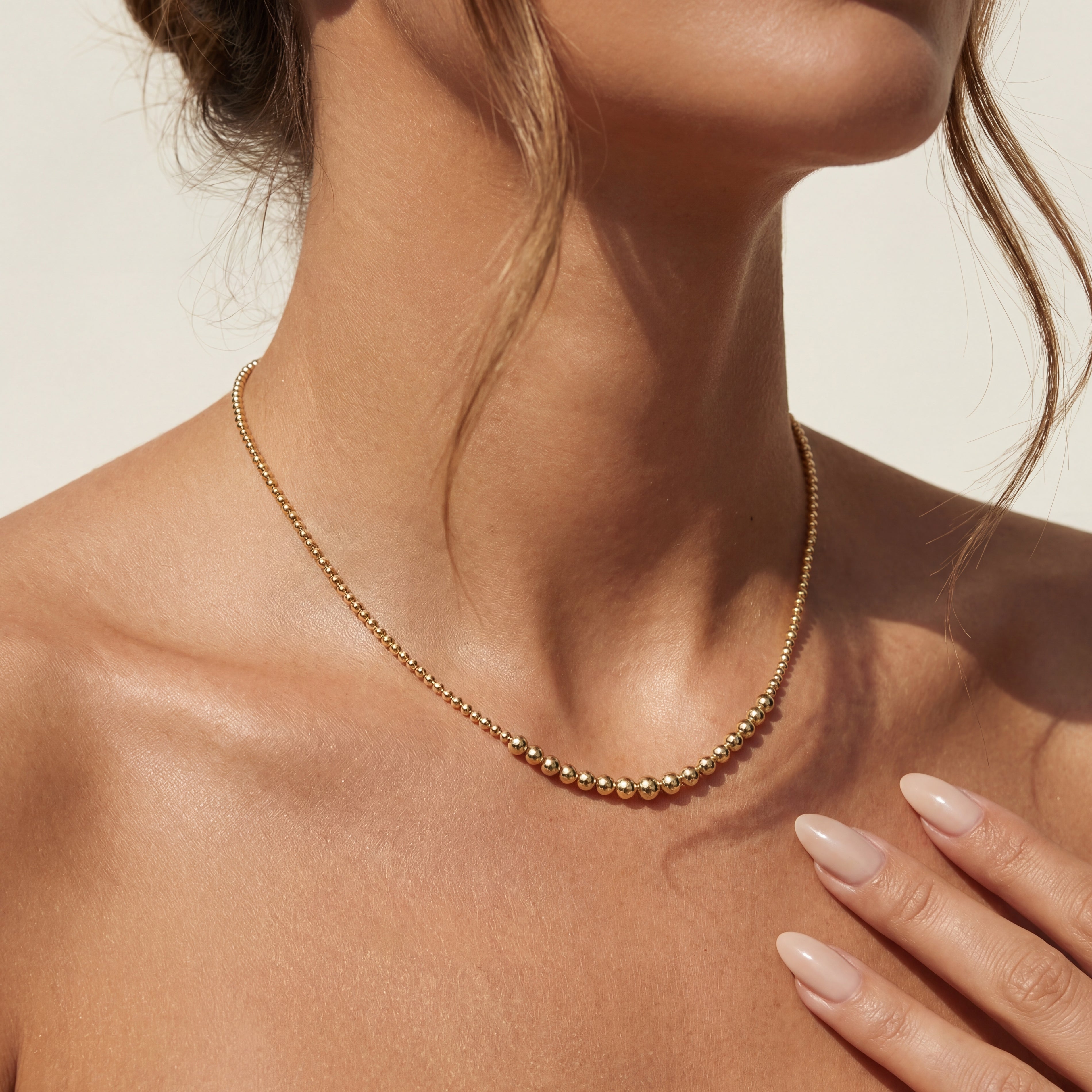 Close-up of a person wearing a gold beaded necklace with a neutral background