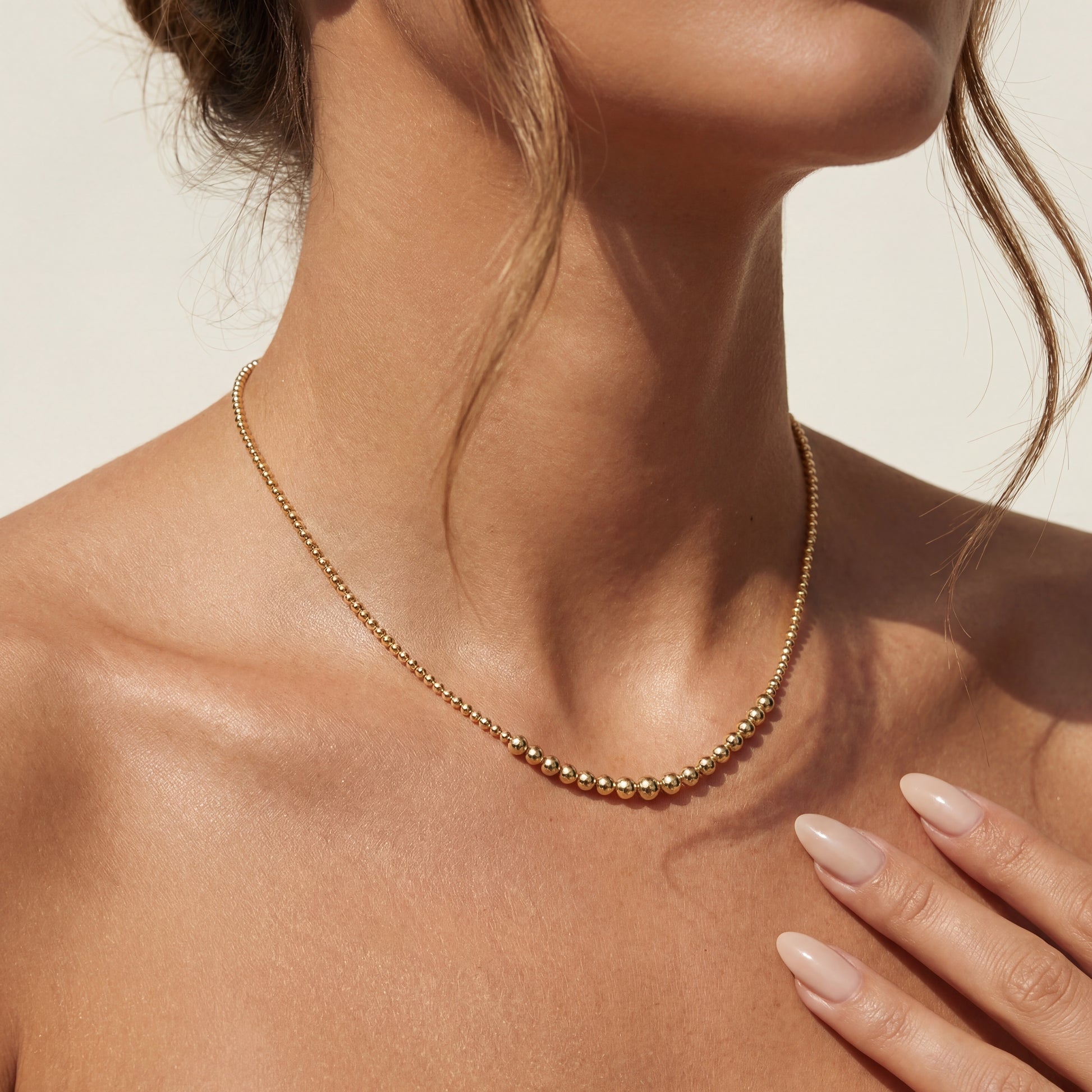 Close-up of a person wearing a gold beaded necklace with a neutral background