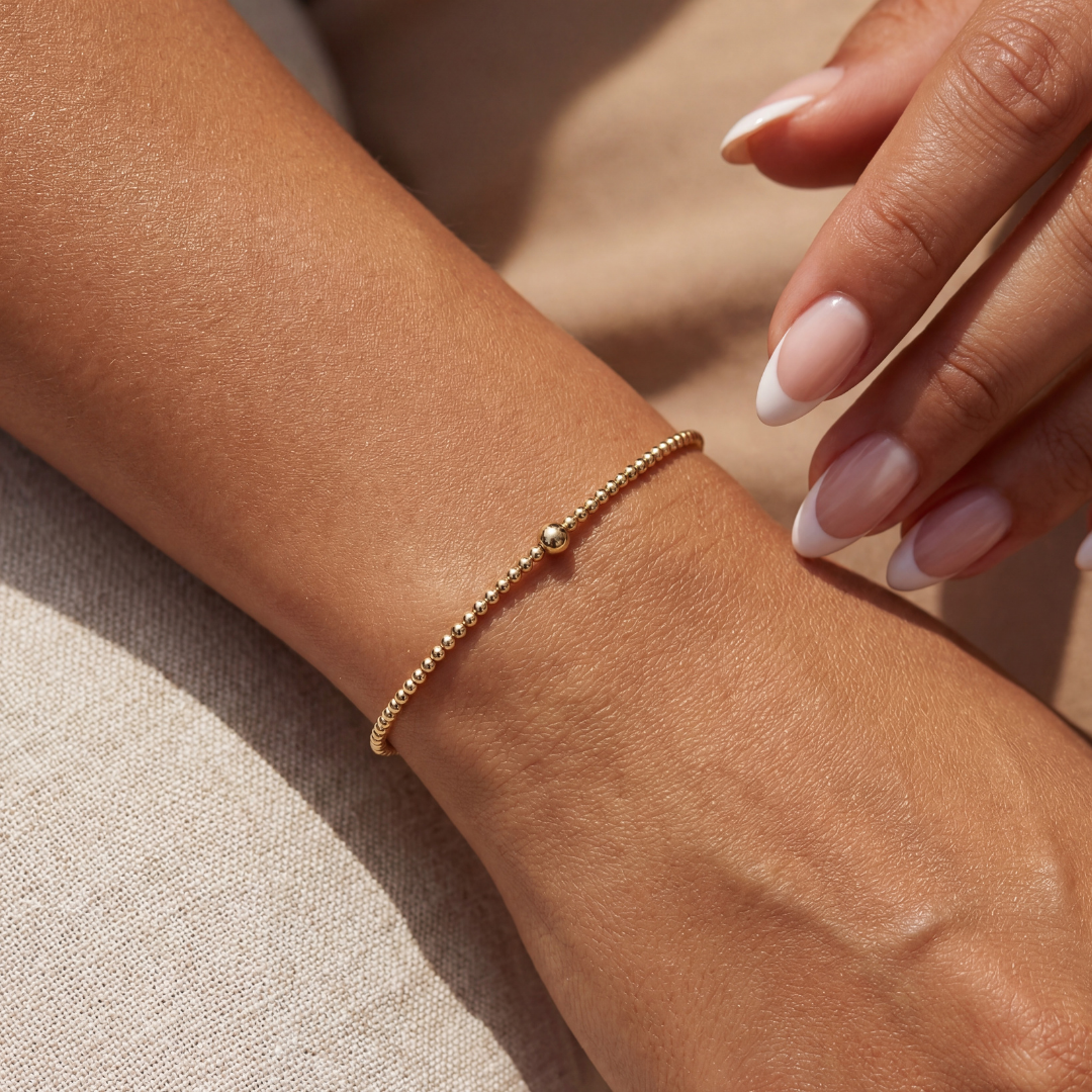 Gold beaded bracelet on a wrist with a neutral background