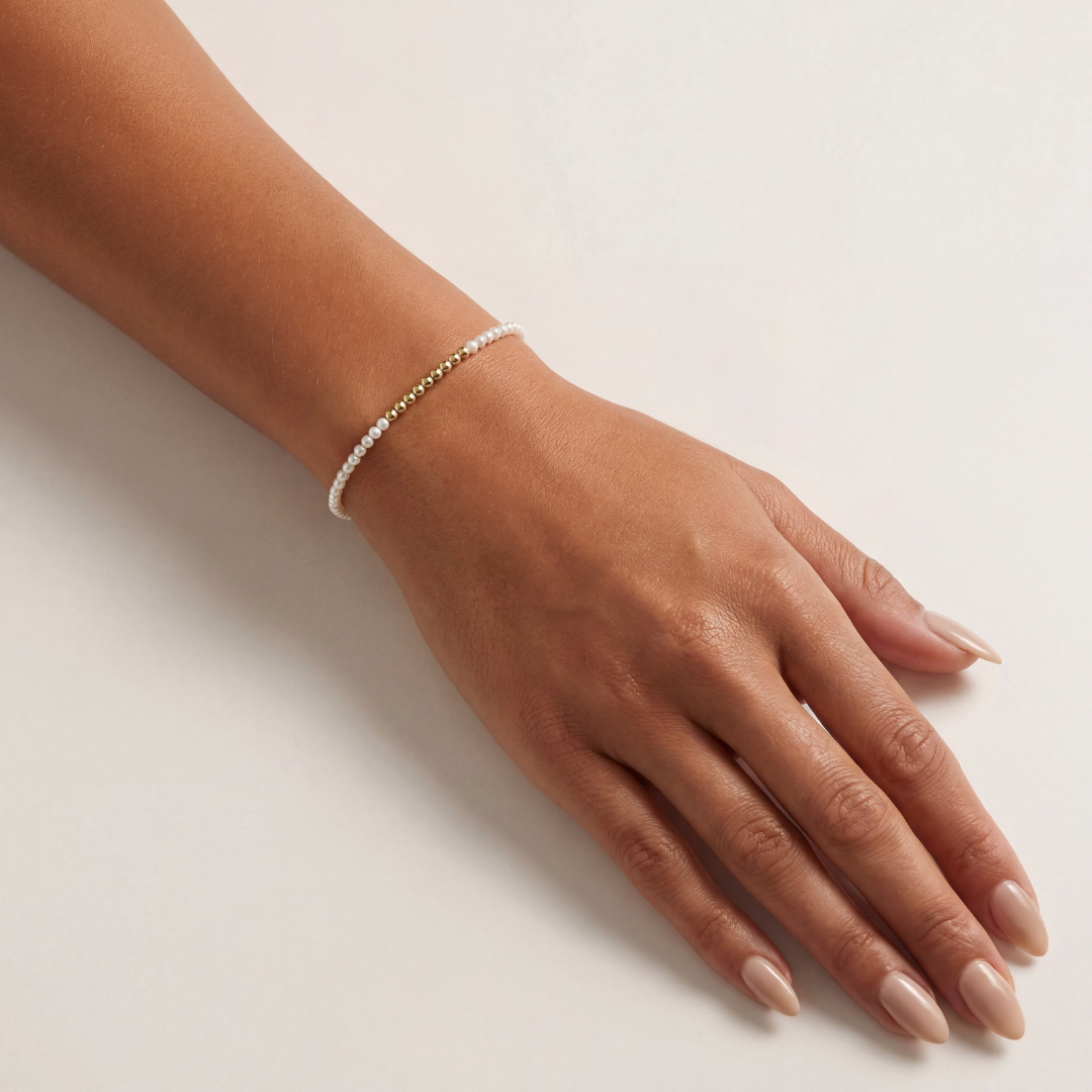 Hand wearing a delicate beaded bracelet on a light background